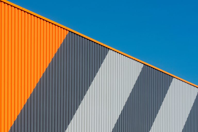 Abstract view of a modern industrial facade with orange and gray stripes under a clear blue sky.