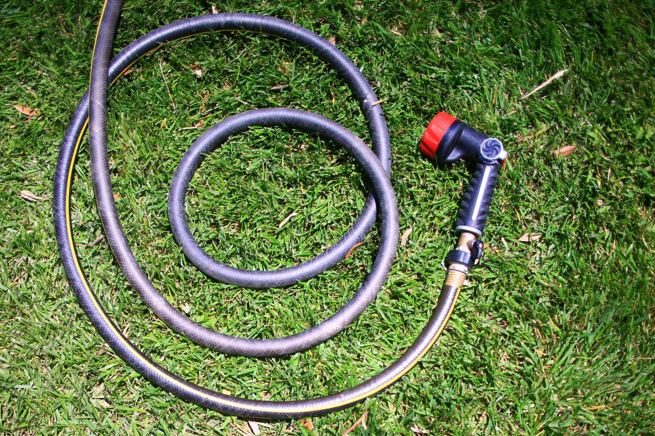 Curled garden hose on lush green grass, shot from above in bright daylight.